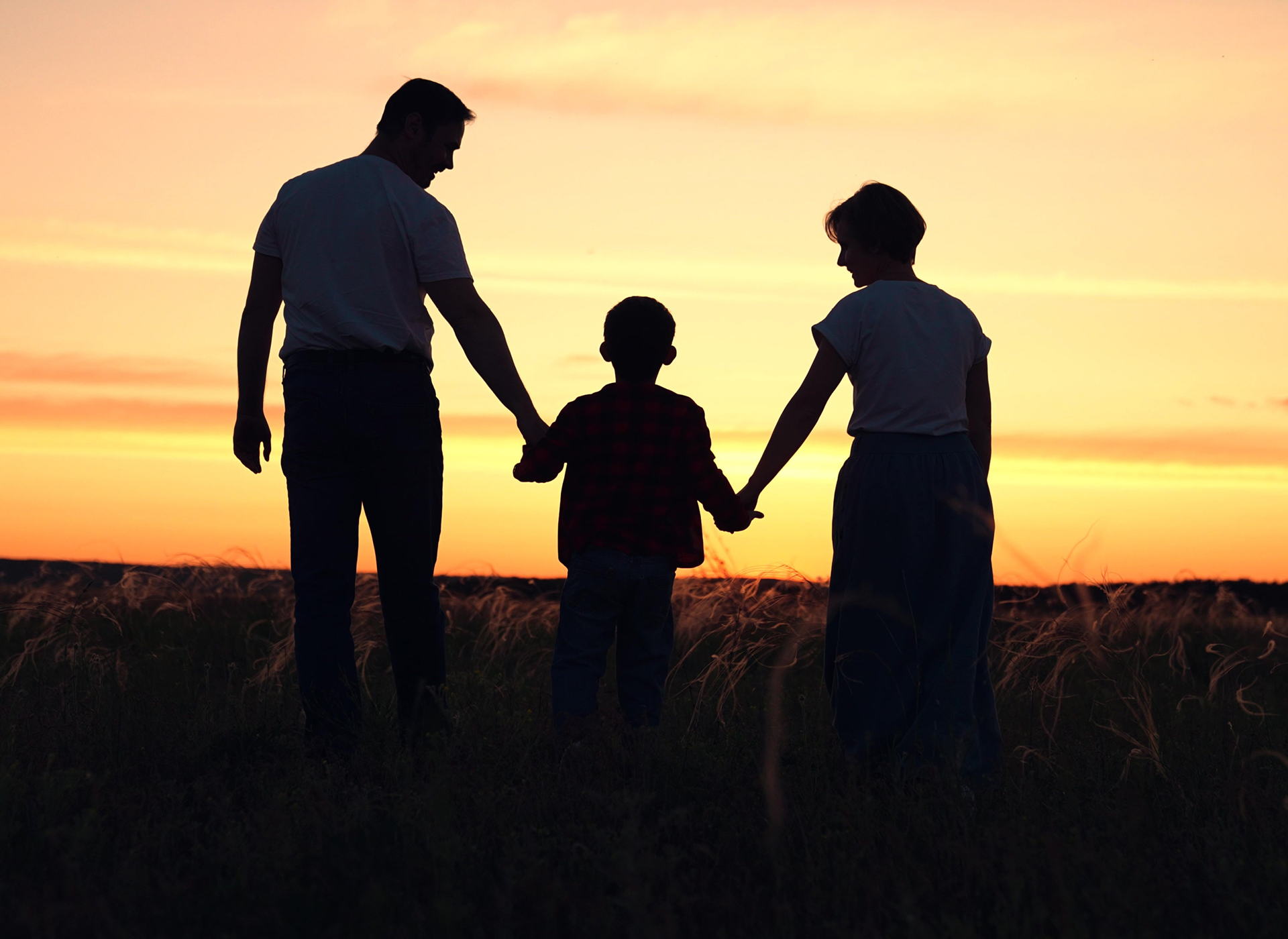 silhouette of man and woman holding little boy's hands in sunset
